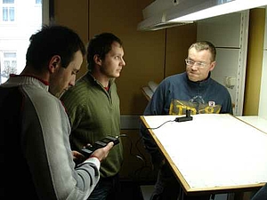 Drei Studenten stehen vor dem Lichtstand und führen Messungen zur Beleuchtungsdichte aus